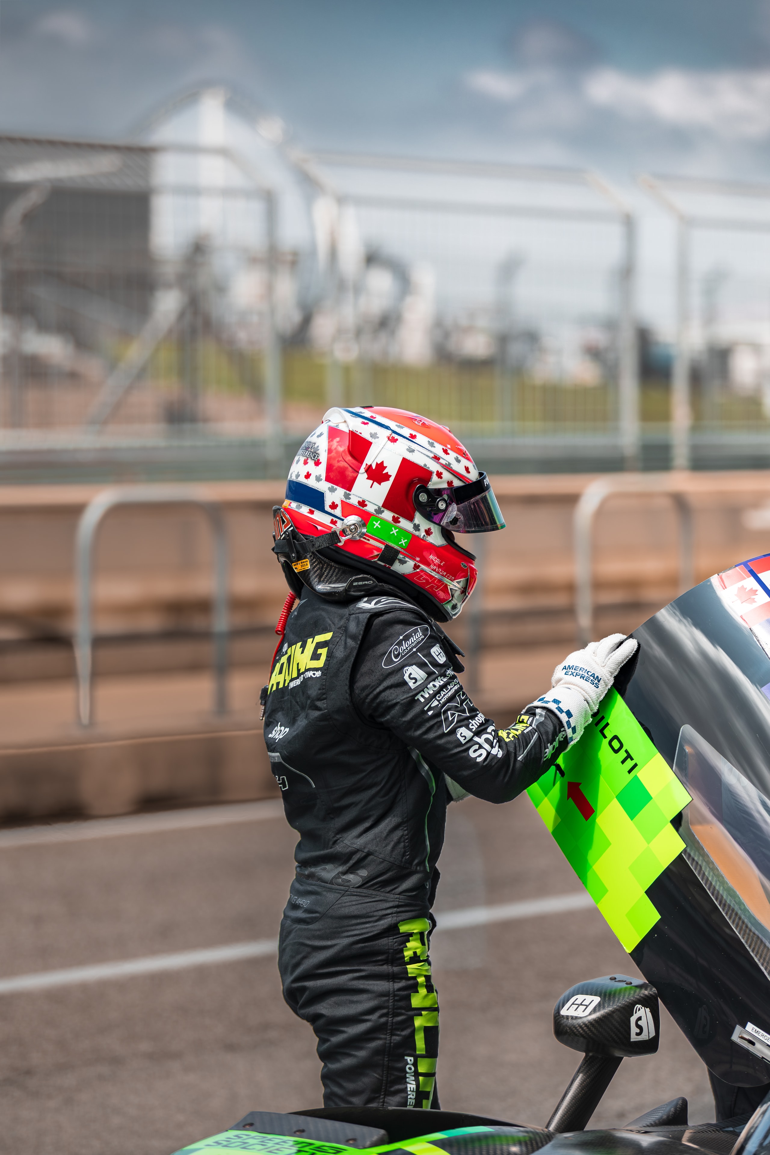 Driver in racing gear standing beside a bright race car